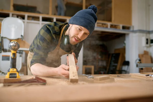年轻的木匠用木板吹锯屑 在现代木工作坊木工 — 图库照片