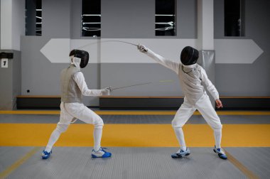 Üniformalı sporcular ve koruyucu kask maskeli adamlar rapier 'larla düello yapıyor. Kılıç ustalığı yarışması konsepti. Dövüş sanatı