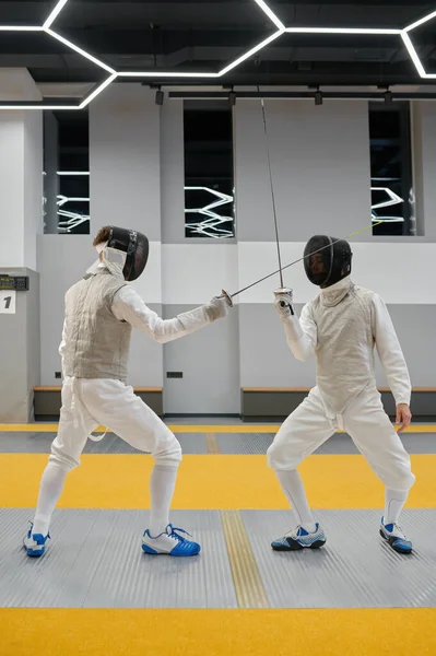 Pair of fencing partners fighting with rapiers practicing attack and defense combination during lesson at martial art club
