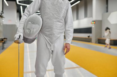 Dövüş sporları okulunun iç kısımlarında eskrim maskesiyle koruyucu miğferini tutan eskrimci manzarası.