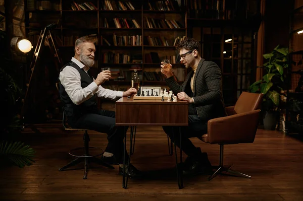 高齢の父と千年の息子は週末に一緒に夜の時間を過ごしながらチェスやウイスキーを飲む — ストック写真