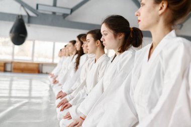 Kimono giyen genç aikido öğrencileri sırada oturuyorlar. Genç spor çocukları grup derslerinin başlamasını bekliyorlar ya da antrenman sırasında antrenörlerini dinliyorlar.