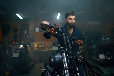 Otomobil tamircisi tamirhanedeki tamirhanede motosikleti hareket ettiriyor. Teknisyen, aracı restorasyon için hazırlıyor.