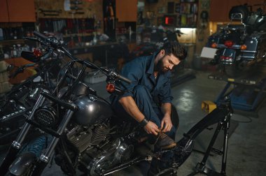 Motosiklet atölyesinin arka plan görüntüsü. Tatil sırasında oto tamircisi dinleniyor. Motosiklette otururken ayakkabı bağcıklarını botlara bağlayan bir teknisyen.