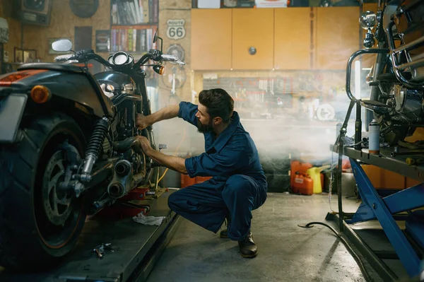 ガレージの修理サービスでオートバイで働く専門的なツールを使用してカバーを身に着けている若い整備士 — ストック写真