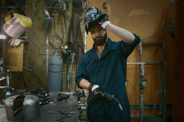 笑顔でカメラを見て保護ヘルメットを脱いでハンサムな若い修理工の肖像画 溶接機で一生懸命働いた後修理サービスマン — ストック写真