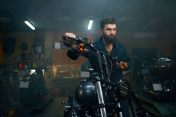 Автомеханик передвигает мотоцикл на ремонтный стенд в мастерской гаража. Специалист-техник готовит автомобиль к реставрации