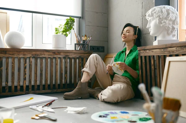 Χαλαρωμένη Νεαρή Γυναίκα Καλλιτέχνης Κάθεται Στο Πάτωμα Μπροστά Από Αξεσουάρ — Φωτογραφία Αρχείου