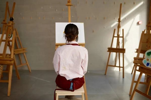 図面を開始するには 空白の白いキャンバスの前に座ってエプロンの若い女性アーティストに戻るビュー アートワークショップトレーニングクラスや自宅の創造的なスタジオのインテリア — ストック写真
