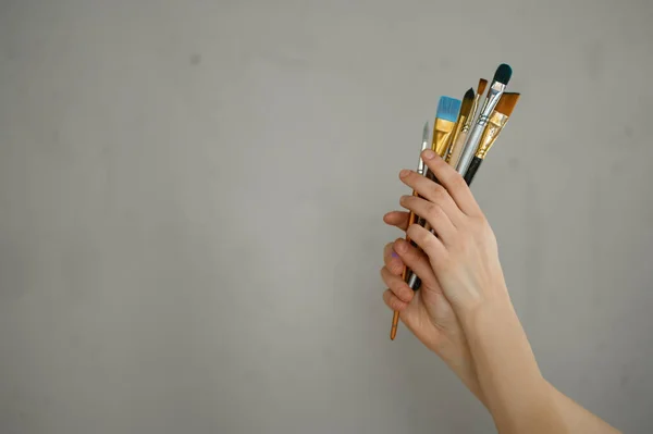 灰色のセメントスタジオの壁の上に絵筆の束を保持女性の手 美術の授業科目の広告コンセプトの基礎資料 — ストック写真