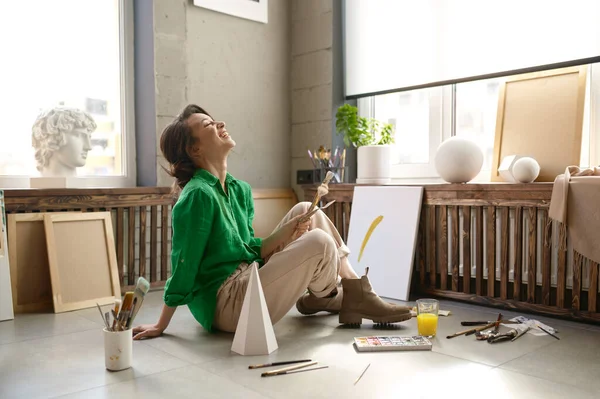Νεαρή Ενθουσιασμένη Γυναίκα Καλλιτέχνης Γελάει Δυνατά Ενώ Κάθεται Στο Πάτωμα — Φωτογραφία Αρχείου