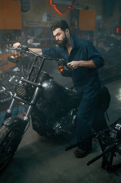 自動整備士は ワークショップガレージで修理スタンドにオートバイを押してください 復旧のための車両を準備する男技術者 — ストック写真