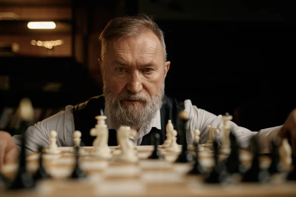 顔の肖像画の自信のあるシニア男見ますチェス作品上のボード上で優しい競争試合中 — ストック写真