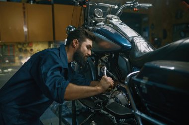 Teknisyen tamir atölyesinde çalışırken ingiliz anahtarı kullanarak motosiklet tamir ediyor. Modern ve klasik motosiklet konseptinin profesyonel bakımı