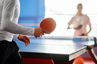 Selective focus on two sportive people playing table tennis indoors. Male and female friendly match clipart