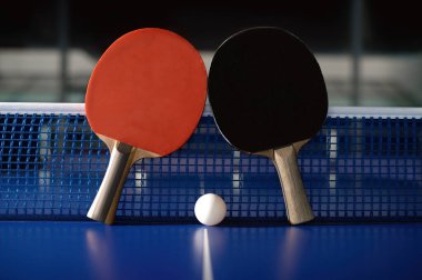 Pair of racket and ball on tennis table against grid net in sport hall. Professional ping pong equipment clipart
