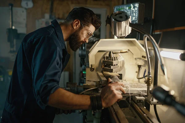 Serviceman working on turning lathe to adjust spare parts. Repair work in workshop