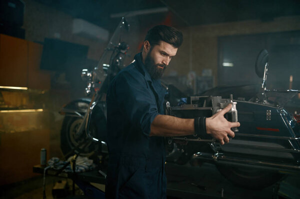 Auto mechanic working on sports bike in authentic workshop garage. Technician carrying motor engine for repair