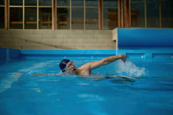 屋内スイミングプールで高速レースを楽しむ運動を行うプロのシニア男性水泳選手 高齢者のためのカーディオスポーツ活動コンセプト — ストック写真