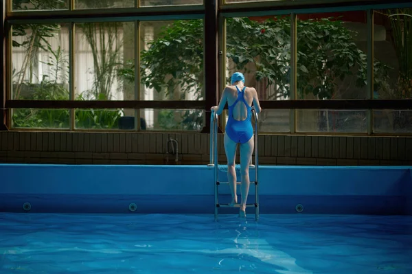 对穿着湿泳衣的女人用梯子从游泳池里出来的倒影 运动游泳训练结束 — 图库照片