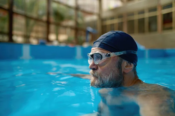 屋内プールでリラックスして退職の休日を楽しむ高齢者の水泳 サイドビューショットのシニア男性水泳頭でキャップと眼鏡 — ストック写真