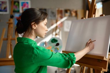 Genç kadın ressam boş tuvali yağlı boyalarla çizmeye ve atölyede fırçalamaya başlıyor.