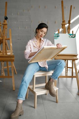 Elinde tuval olan çekici genç kadın ressam boyalarla resim çiziyor ve önünü fırçalıyor. İnsanlar, eğlence ve hobi konsepti