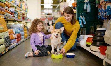 Mutlu anne ve kız evcil hayvan dükkanında Corgi köpeklerini besliyor.