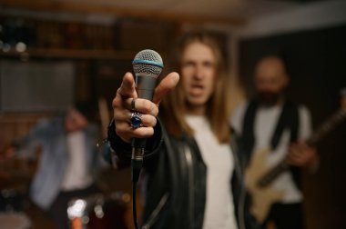 Kulüpte rock grubu performansı. Siyah ceketli ve beyaz tişörtlü neşeli erkek rockçı dinamik mikrofon tutan seyirciyi işaret ediyor.