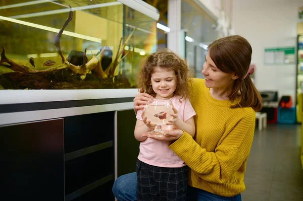 幸せな母親と小さな娘の肖像画はペットショップで魚を買った — ストック写真