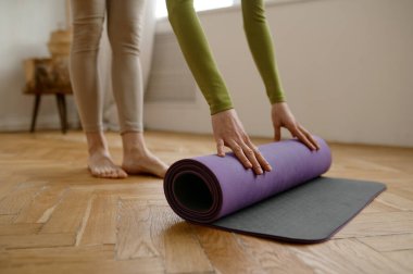 Yakın plan kadın, sabah meditasyonu ya da aktif fitness çalışması için ahşap zeminde yoga minderi yuvarlıyor.