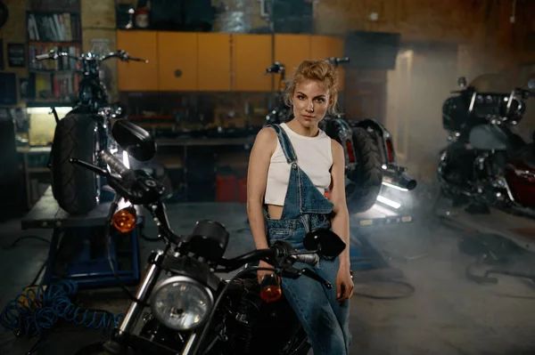 Молодая Женщина Джинсовом Комбинезоне Смотрит Камеру Позирующую Мастерской Мотоцикла Концепция — стоковое фото