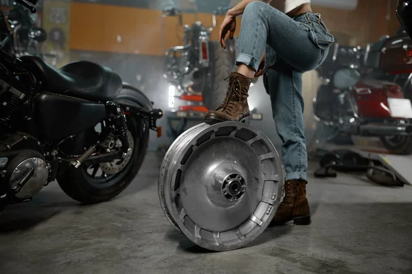 クロムホイールディスク上の女性保持脚とオートバイガレージワークショップで撮影作物 — ストック写真