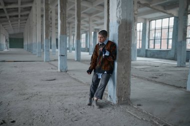 Evsiz, serseri, sigara içen genç bir kadın ayakta zor duruyor beton destek sütununa yaslanmış yorgun, aç ve üşümüş hissediyor.