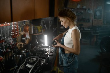 Atölyede çalışan güzel bir kadının yan görüntüsü. Genç profesyonel kadın teknisyen motosikletin müşteri süspansiyon motor sistemini tamir ediyor.