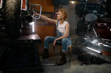 Özel motosikletle sorunu çözmeye çalışan düşünceli genç bir kadın. Akşamları atölye içi