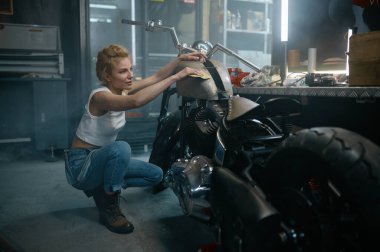 Atölyede tamirat yaptıktan sonra motorsiklet yakıt deposunu cilalayan oldukça memnun genç bir kadın.