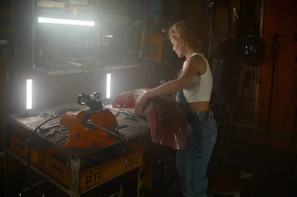年轻美丽的女机修工晚上在车库里修理钢制摩托车零件 — 图库照片