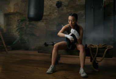 Atletik genç bayan boksör ellerinde bandajlarla spor salonunda dövüşmeye hazırlanıyor.