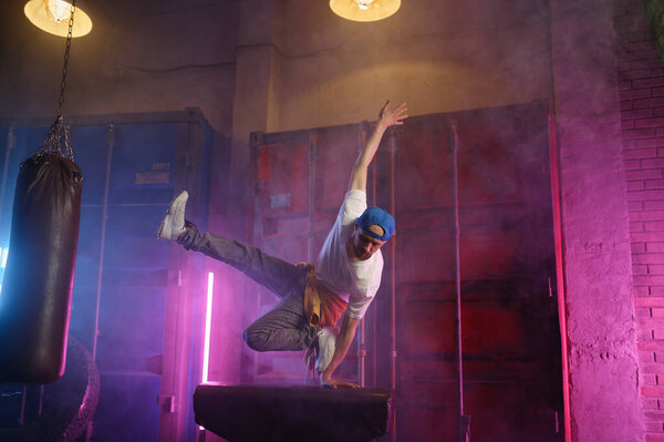 Молодой парень хип-хоп исполнитель брейк-данс в неоновом свете клуба прыгает через спортивный гимнастический аппарат. Танцовщица