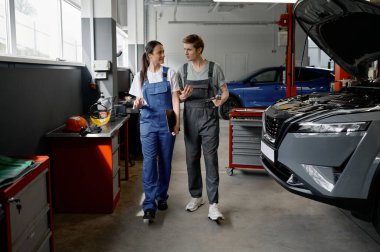 Erkek teknisyen ve kadın tamirci, bozuk müşteri arabasının yanında yürüyor. Araba servisi garaj konseptinde.