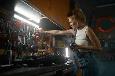 Akşamları atölyede motorsikletin yedek parçasını tamir eden genç bir kadın. Güzel bayan teknisyen, alet edevat ve ingiliz anahtarıyla çalışıyor.