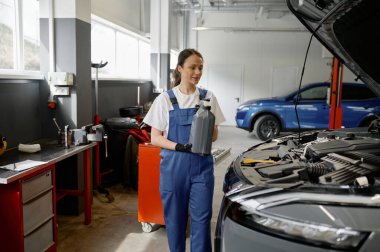 Genç bir kadın arabaya servis yaparken plastik şişe taşımak için yeni motor yağı hazırlıyor.