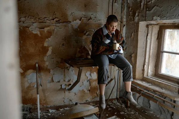 无助的年轻女子可以坐在废弃的房间里吃着炸弹 绝望地看着窗外 — 图库照片