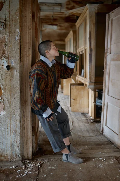 无家可归的女人喝着瓶子里的啤酒住在废弃的房子里 乞讨和酗酒概念 — 图库照片