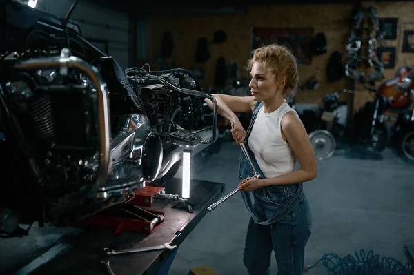 ガレージでオートバイを修復するために作業ツールを使用して青いジャンプスーツを身に着けている才能のある女の子 創造的な本物のワークショップでの情熱的な若い女性 — ストック写真