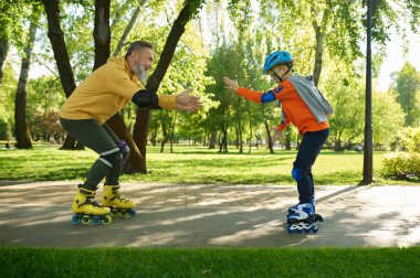 Dedem şehir parkında paten sürmeyi öğretiyor. Mutlu aile eğleniyor ve açık havada spor yapıyor.