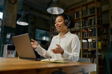 İnternette çalışan ve dizüstü bilgisayara bakan kulaklık takan kadın bir ofis çalışanı. Eğitimsel webinar izlemek, müşteriyle video görüşmesi yapmak, ortak konseptiyle sanal görüşme