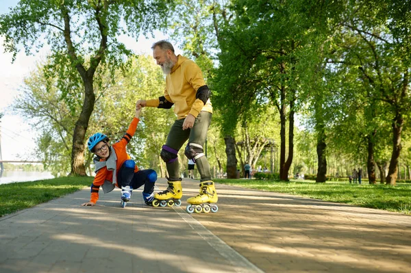 Senior man roller skating with little boy in urban park. Cheerful grandfather catching grandson falling upside down. Happy parenting and childhood