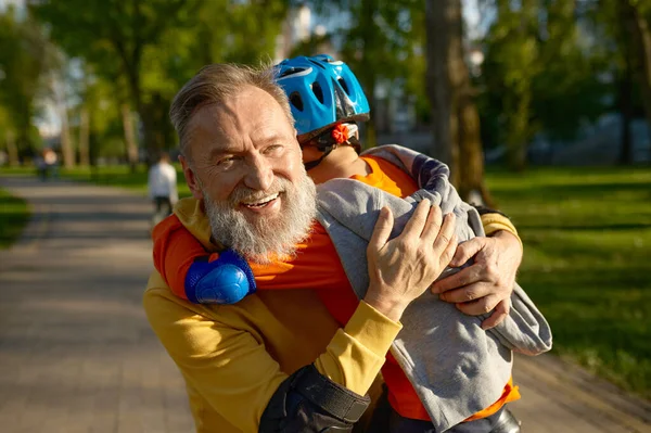 Portrait of loving grandparent hugging adorable grandson. Happy family and roller skating in park on weekend